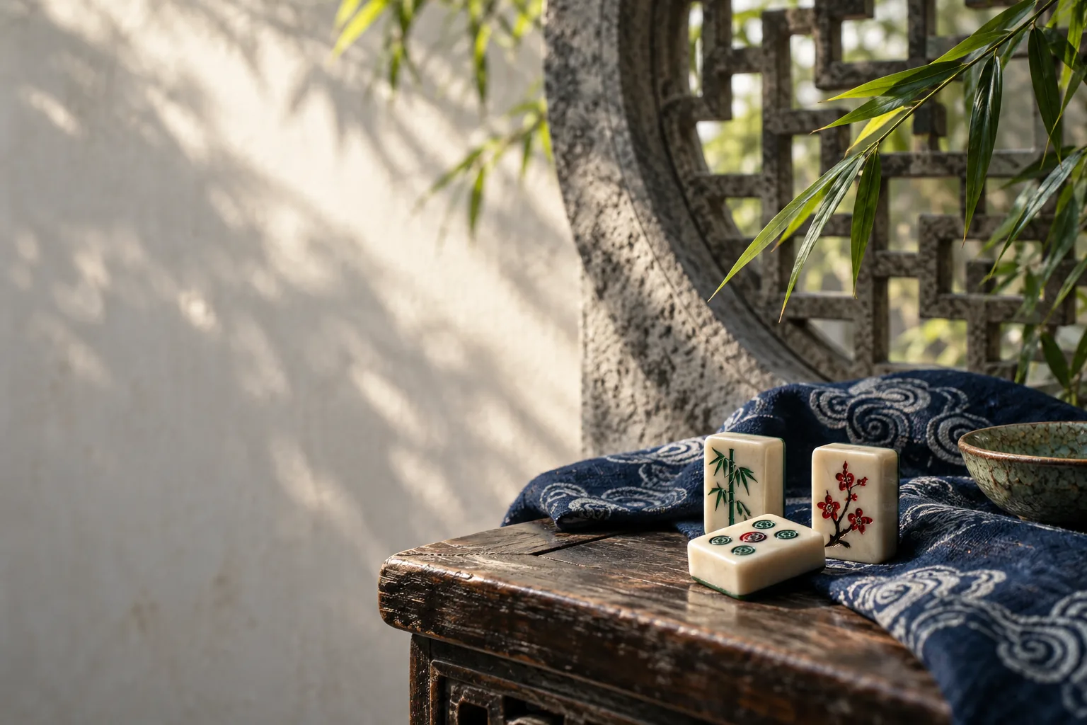 Mahjong tiles, indigo textile, bamboo, and a carved stone window in soft daylight
